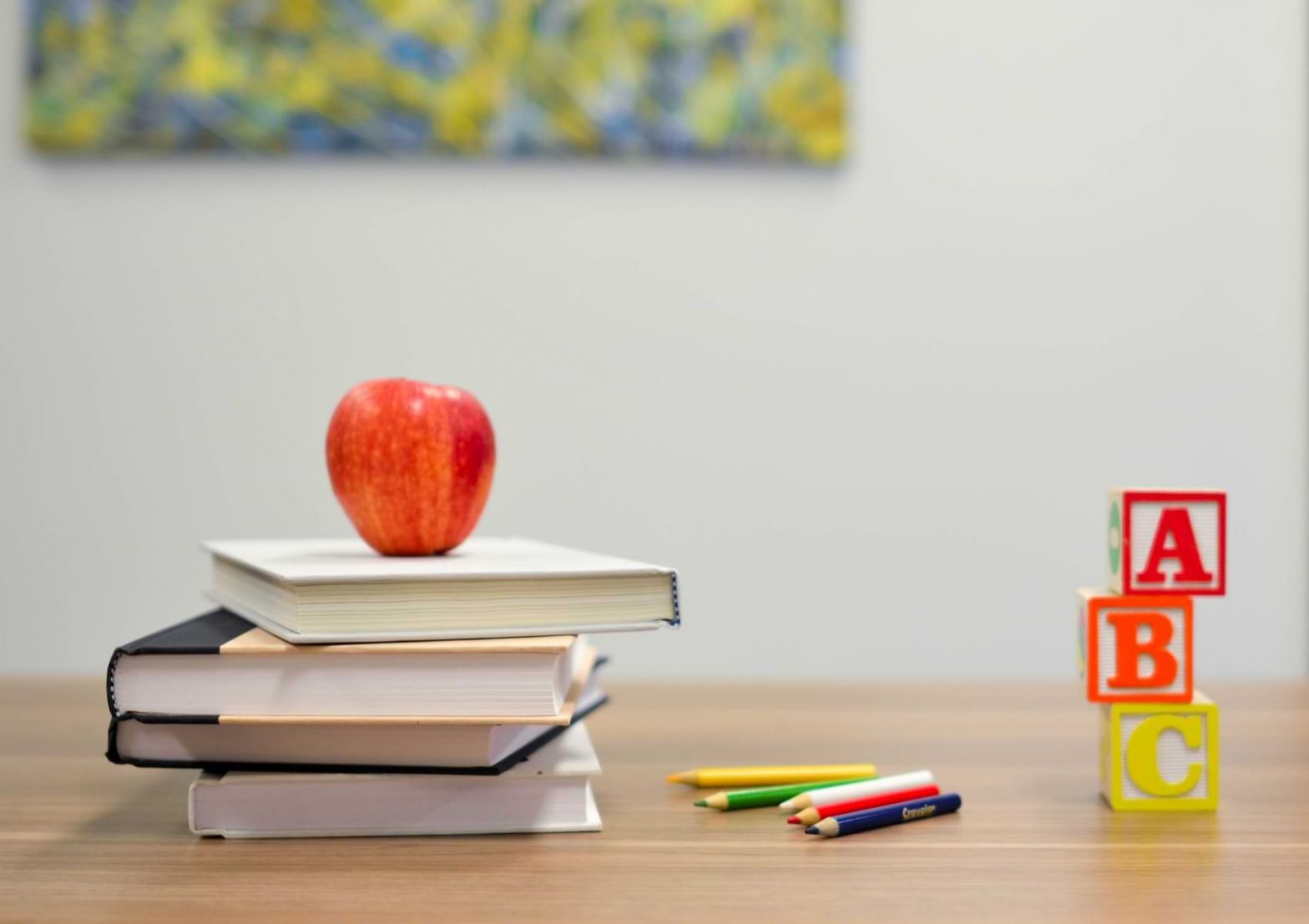 A desk is crowded with books, blocks, pencils and an apple, classic back to school materials