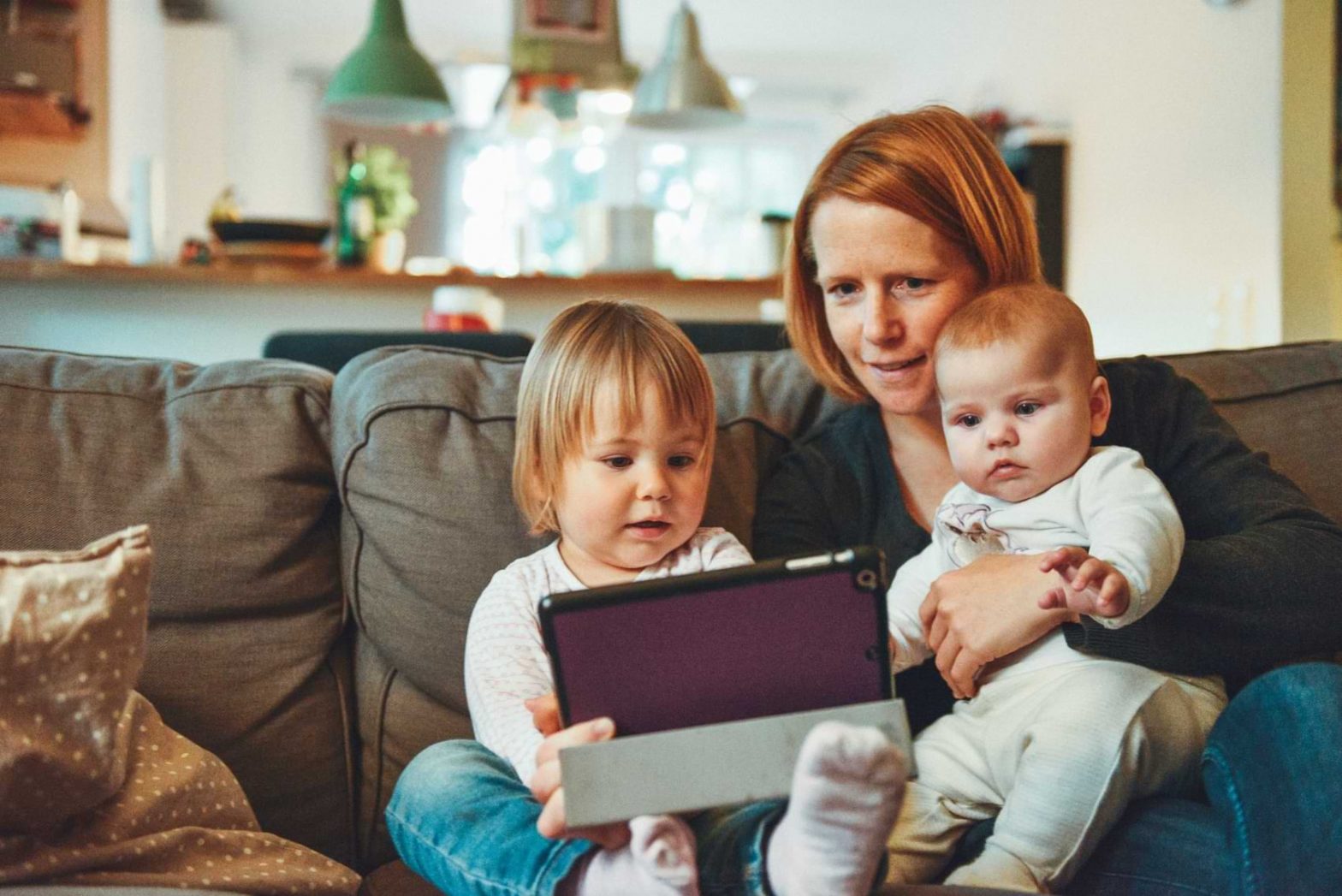 A mother and her two children sit together to watch TV on a tablet.