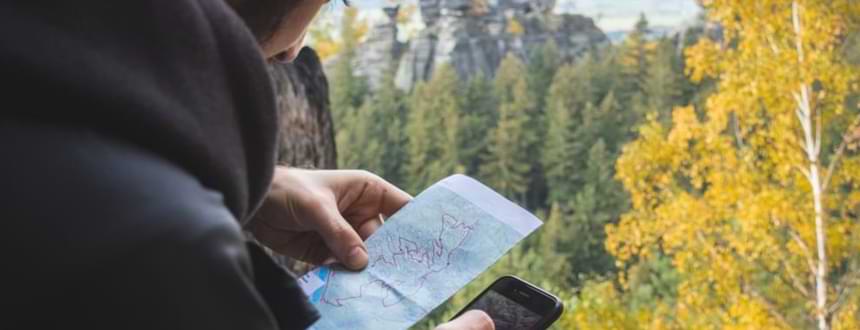 A man looks at his phone and a map, using some of the best travel apps to help him out during his travels.