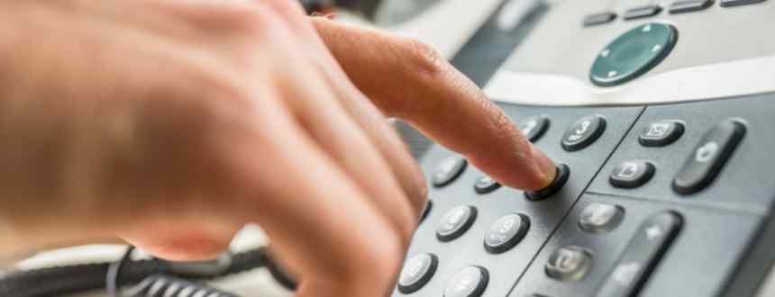 A closeup of a hand using a landline phone, whose number could be transferred to a mobile phone via phone porting.